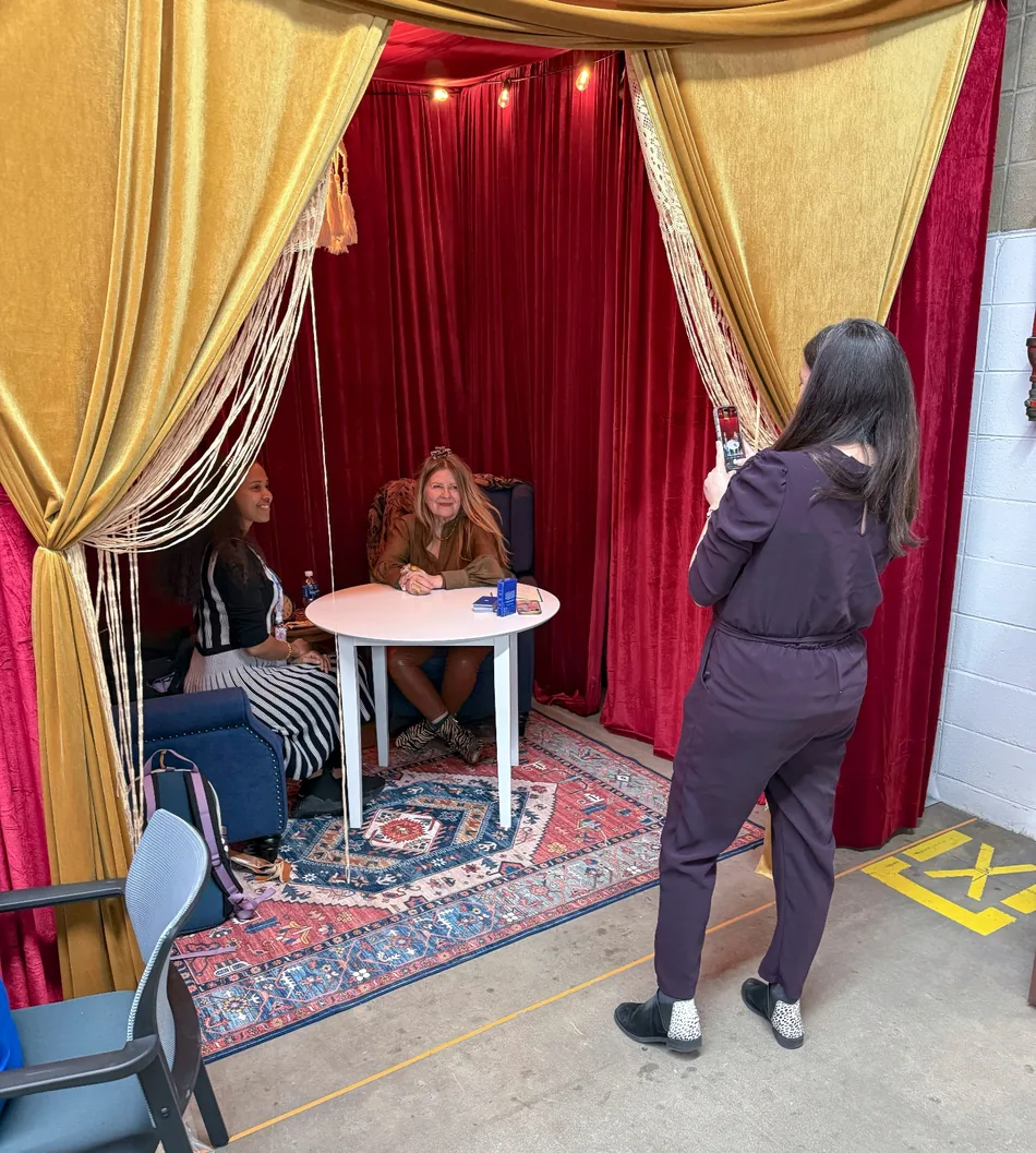 The Reserve booth at ETH Denver: a curtained gold-and-red tent with a tarot reader at a small table, a visitor seated opposite her, and the deck on the table.